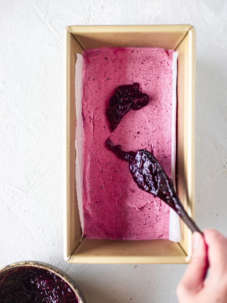 Spreading jam on the raspberry layer of the berry ice cream cake